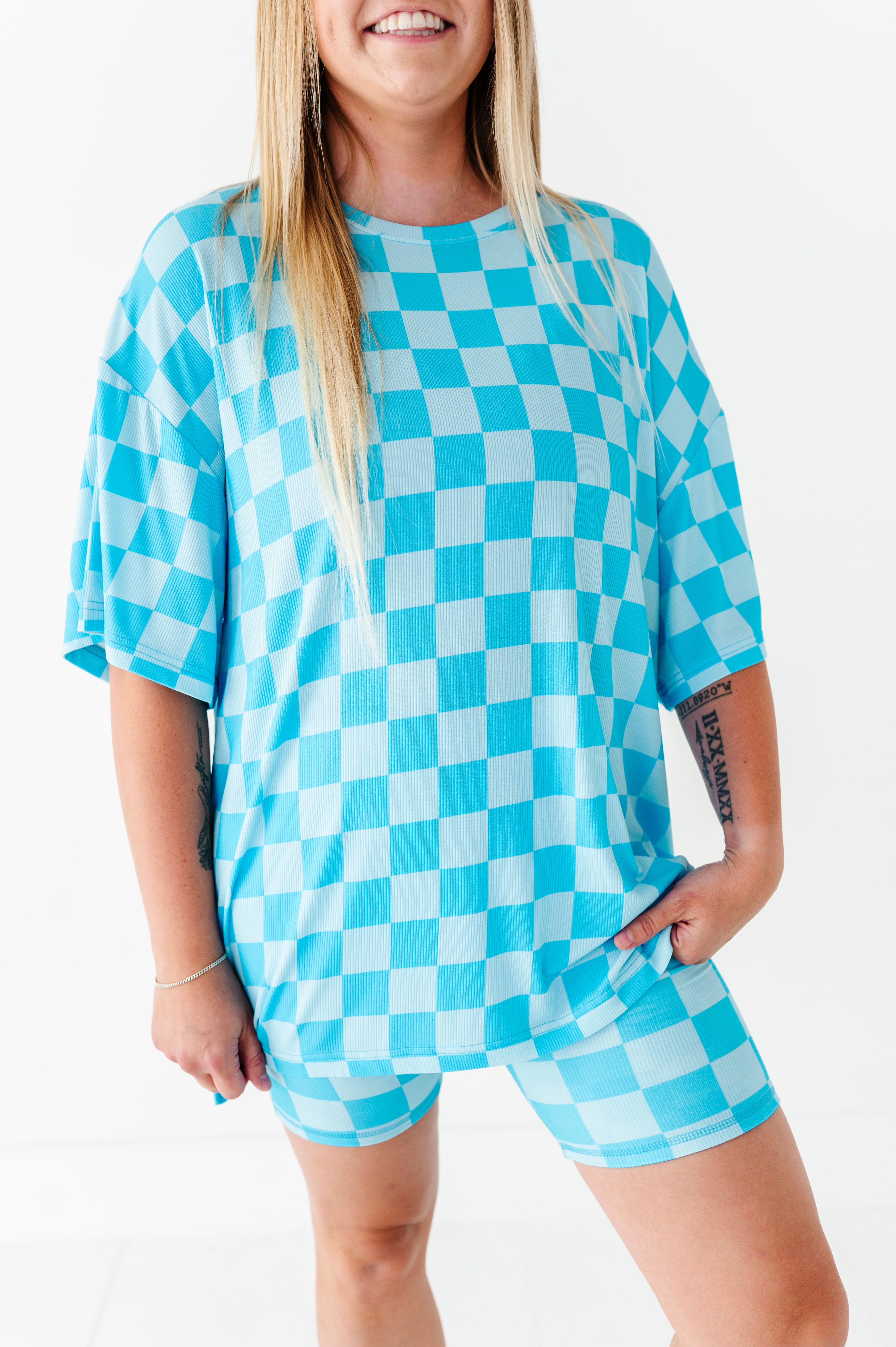 A woman wearing an oversized short-sleeve t-shirt and matching shorts in a bright blue and white checkerboard pattern, photographed against a clean white background.